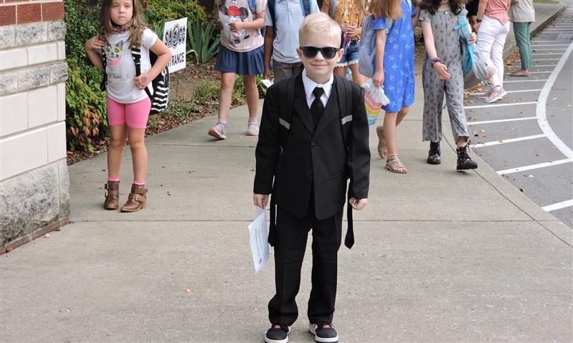 A boy wearing a suit and sunglasses smiles